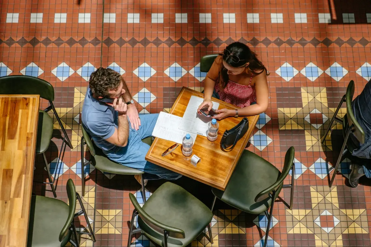 Two people at a café table on a patterned tile floor, seen from above, with menus and phones