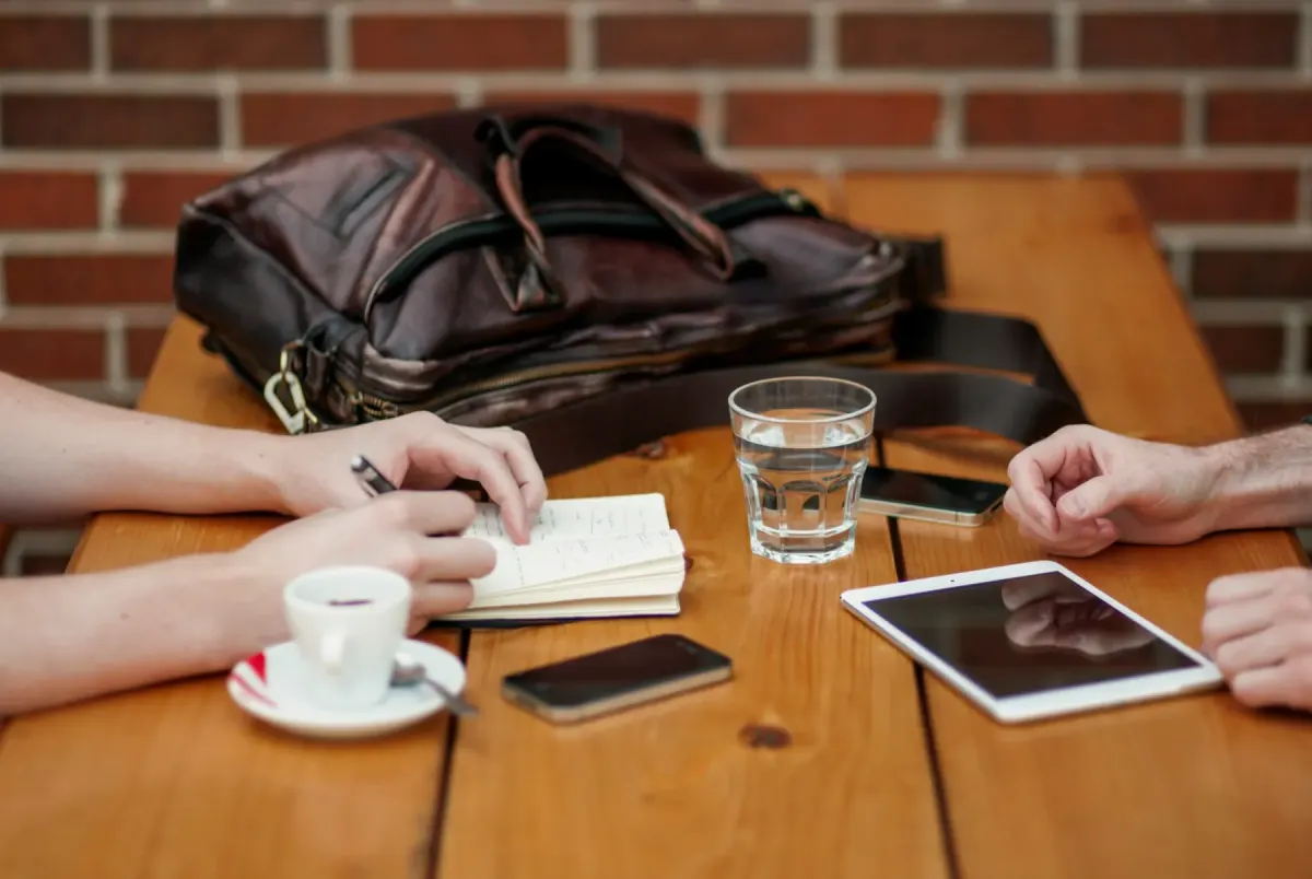 Two people meeting at a café table with a notebook, coffee and a tablet