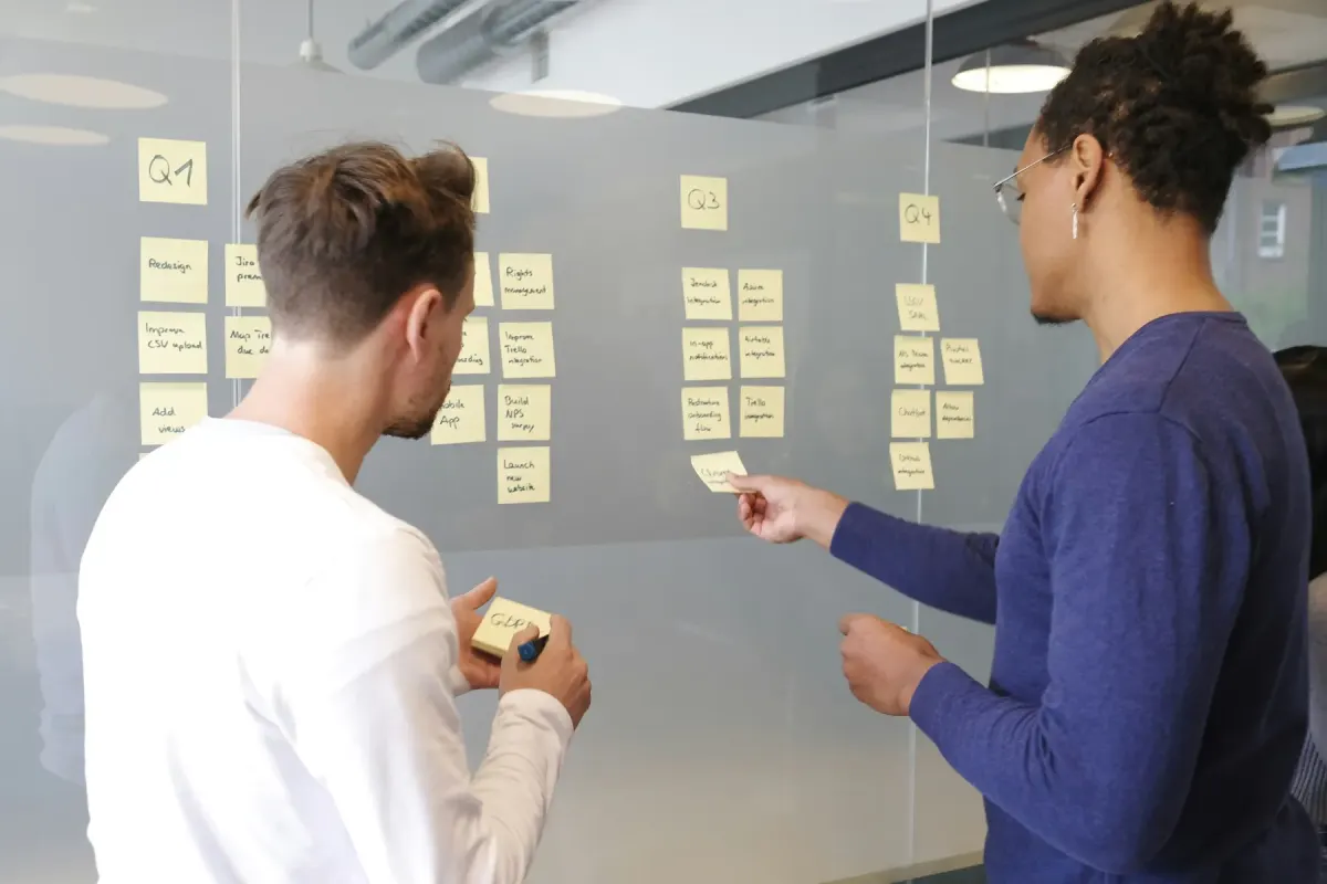 Two colleagues sorting sticky notes into quarterly columns on a glass wall