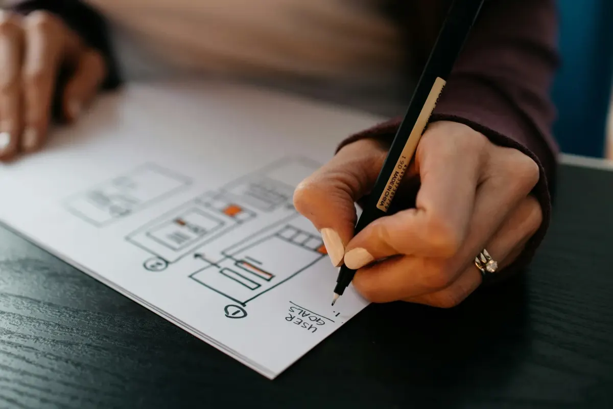 Hands sketching website wireframes and a user flow on paper